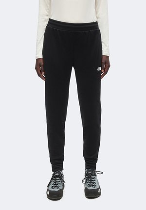 Person wearing black The North Face jogger pants and gray hiking shoes standing against a plain background.