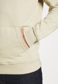 Beige genser med rund hals, sidelommer, ribbestrikkede mansjetter og hem. En myk tekstur med synlige sømdetaljer.