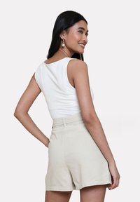 Top bianco senza maniche con una texture liscia, abbinato a pantaloni corti beige a vita alta. Il modello è visto da dietro, mostrando il design dell'outfit.