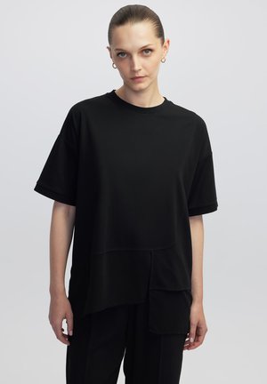 Zwart oversized t-shirt van zachte stof, met korte mouwen, een ronde halslijn en een gelaagd ontwerp met verschillende lengtes en texturen.