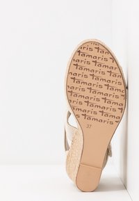 Semelle de sandale compensée beige avec talon tressé, semelle extérieure en caoutchouc texturé avec le logo "Tamaris", taille 37 indiquée sur la semelle.