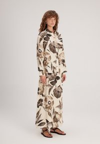 Ensemble imprimé floral avec un col, présentant des tons beige et marron. Le tissu est léger, associé à des sandales noires.