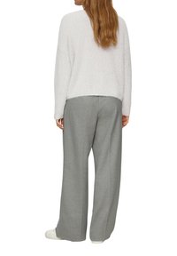 Witte gestructureerde trui en lichtgrijze brede broek met subtiele patronen, een relaxte pasvorm en witte sneakers.