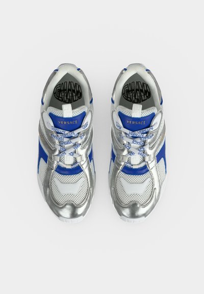 Paire de baskets Versace en argent, bleu et blanc, avec des lacets marqués et un logo sur les languettes bleues, vues de dessus.