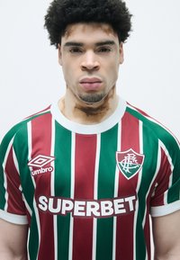 Sarkans un zaļš svītrots futbolbikses krekls ar baltām akcentiem, kurā redzams "SUPERBET" logo, Umbro emblema un komandas nozīmīte uz krūtīm.