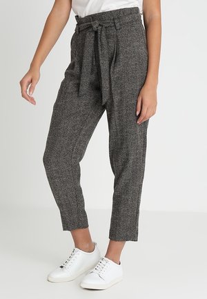 High-waisted houndstooth trousers in gray with a fabric belt. Textured material, tapered legs, and side pockets. Paired with white sneakers.