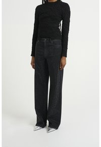 Top negro de textura con mangas largas combinado con vaqueros negros de cintura alta con destellos plateados, complementado con zapatos metálicos de punta. 