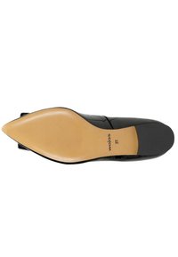 Chaussure noire à bout pointu avec une finition brillante, présentant un dessus noir lisse, une semelle beige et une texture subtile sur la surface de la semelle.