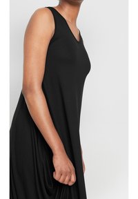 Czarna sukienka bez rękawów z dekoltem w kształcie litery V, wykonana z gładkiego, zwiewnego materiału; posiada drapowania z boku i luźny krój.