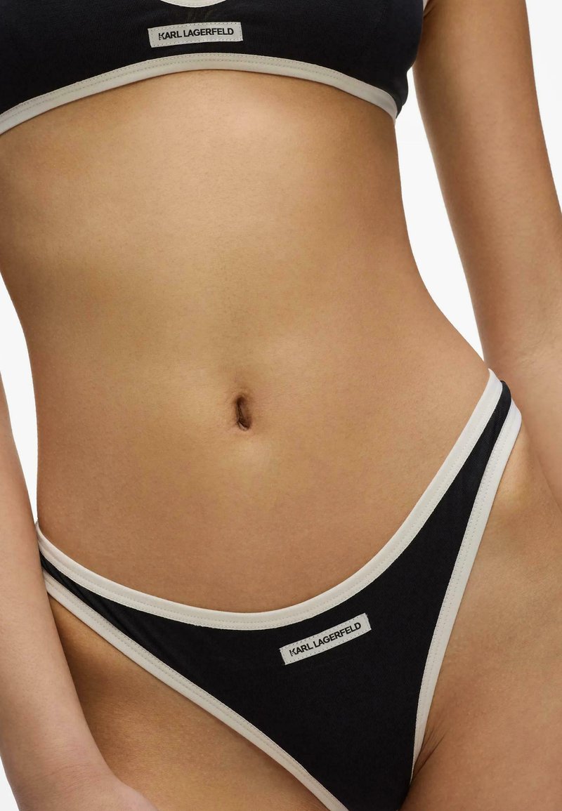 Gros plan sur la taille d’une personne portant des sous-vêtements et un soutien-gorge de sport noirs et blancs de la marque Karl Lagerfeld.