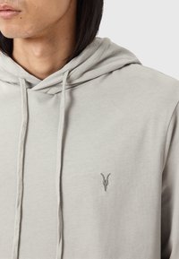 Hoodie gris en tissu doux, avec une poche kangourou, un capuchon avec cordon de serrage et un petit design brodé d'un crâne de chèvre sur la poitrine.