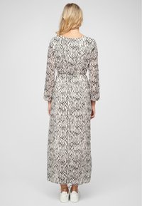 Robe longue et légère avec un motif de vagues noir et blanc, resserrée à la taille, dotée de longues manches et d'un col rond. Portée avec des baskets blanches.