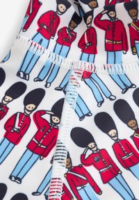 Tissu à motifs présentant des gardes de cartoon en uniformes rouges et pantalons bleus, avec des chapeaux noirs ronds distincts. Détails de couture visibles inclus.