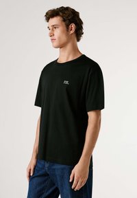 Camiseta de algodón negra con cuello redondo, mangas cortas y un pequeño logo blanco "PJL" en el pecho izquierdo.