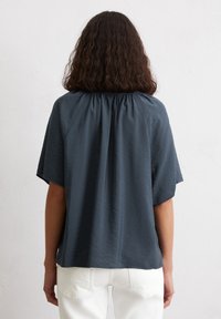 Top blu navy a maniche corte con scollo arricciato, tessuto morbido e dalla vestibilità rilassata. Design minimalista senza chiusure visibili.