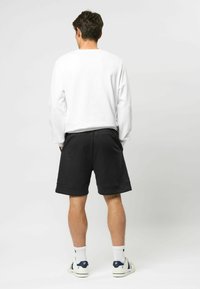 Witte lange mouwen sweatshirt en zwarte shorts, met een relaxte pasvorm. Zwarte shorts hebben omgeslagen zomen. Witte sneakers met gekleurde accenten.