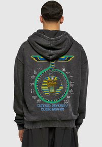 Kullsvart hettegenser med et fargerikt grafisk design av en elefant og egyptiske motiver, med teksten "World Slavery Tour 1984-85." Myk tekstur.
