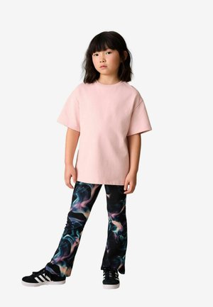 Różowy, luźny t-shirt zestawiony z czarnymi legginsami ozdobionymi kolorowym, abstrakcyjnym, wirującym wzorem. Stylizację uzupełniają czarne trampki.