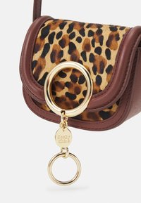 Hnědá kožená taška s leopardím potiskem na klopě, zlatými detaily a kulatým kroužkem na klíče. Vyznačuje se hladkým povrchem a odvážnými vzory.