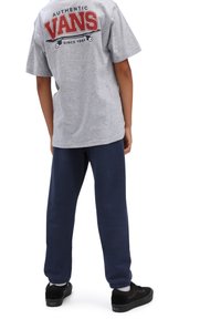 Grau Baumwoll-T-Shirt mit rotem "VANS"-Logo, kombiniert mit marineblauen Jogginghosen und schwarzen Turnschuhen. Lockere Passform mit kurzen Ärmeln und gerippten Bündchen.