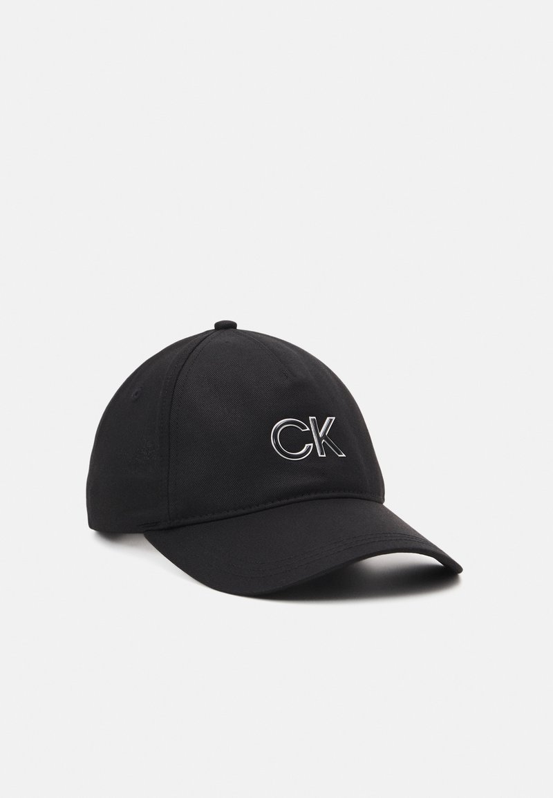 Casquette de baseball noire avec une visière incurvée et un logo blanc "CK" brodé à l'avant, sur fond blanc uni.