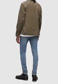 Olivgrön jacka i bomull med rak passform, kombinerad med ljusblå smala jeans och svarta ankelstövlar.