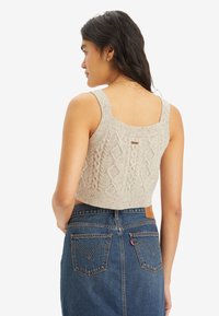 Beige cropped knit tank sweater with textured cable pattern and wide straps, paired with a high-waisted denim skirt featuring back pockets.