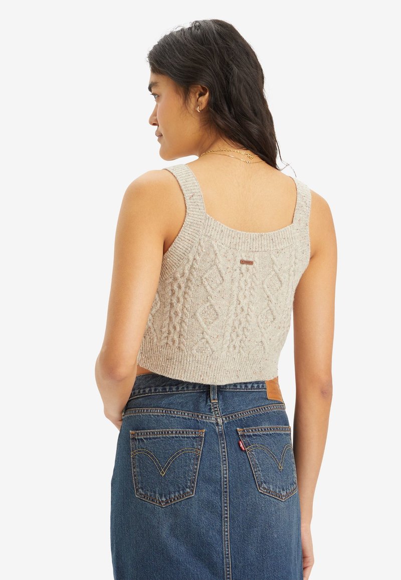 Top corto in maglia beige con motivo a treccia testurizzato e spalline larghe, abbinato a una gonna di jeans a vita alta con tasche posteriori.