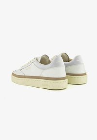 Sneakers bianchi in pelle con una linea di accento beige, suole in gomma testurizzata e design minimalista. Presentano il branding sul tallone e sulla linguetta.