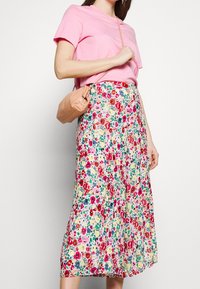 Jupe midi fleurie avec un motif rose clair, rouge et vert sur fond crème, associée à un t-shirt rose uni et un petit sac beige.