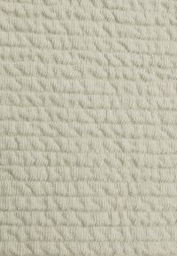 Texturovaná látka v barvě off-white s vzorovanými vyvýšenými pleteninami a nepravidelným povrchem, což vytváří měkký a útulný vzhled.