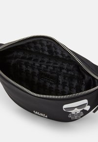 Zwarte pouch met een gladde buitenkant, zilveren rits en gestreepte zwarte voering. Voorzien van grafisch ontwerp aan de voorkant met een karakterillustratie.