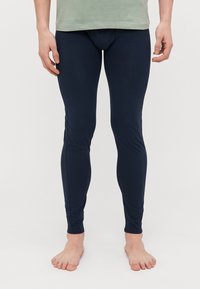 Marinblå leggings gjorda av mjukt, stretchigt tyg med en smal passform, designade för komfort och flexibilitet, bärs med en ljusgrön topp.
