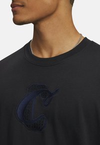 Sort bomulds-sweatshirt med et stort mørkeblåt broderet "C"-logo på brystet, rund halsudskæring og korte ærmer.