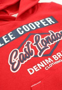 Sweat à capuche rouge avec "Lee Cooper" en lettres blanches sur fond marine, script en cursive "East London", et texte "Vêtements de marque en denim".