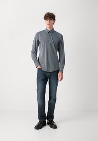 Modra in bela srajca z dolgimi rokavi s ovratnikom, zapiranje na gumbe, v kombinaciji s temno modrimi jeans hlačami in črnimi čevlji. Preprost dizajn in teksture.