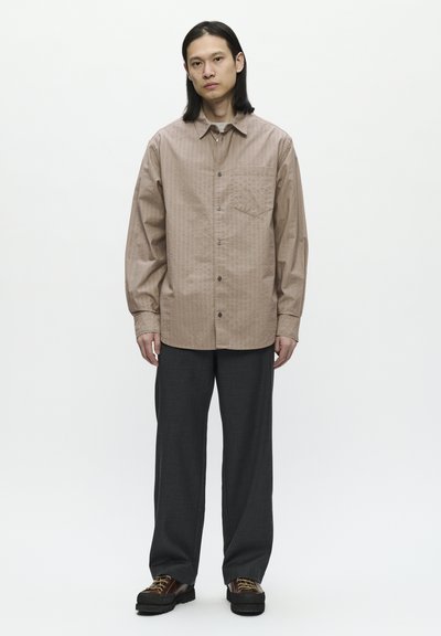 Camisa de botones color marrón claro con un patrón texturizado, de manga larga y bolsillo en el pecho, combinada con pantalones rectos gris oscuro y zapatos negros.