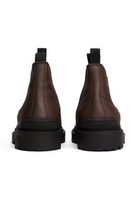 Botas de tobillo de cuero marrón con un acabado texturizado, paneles laterales elásticos y una suela de goma negra con detalles de dibujo. Logo de la marca en el talón.