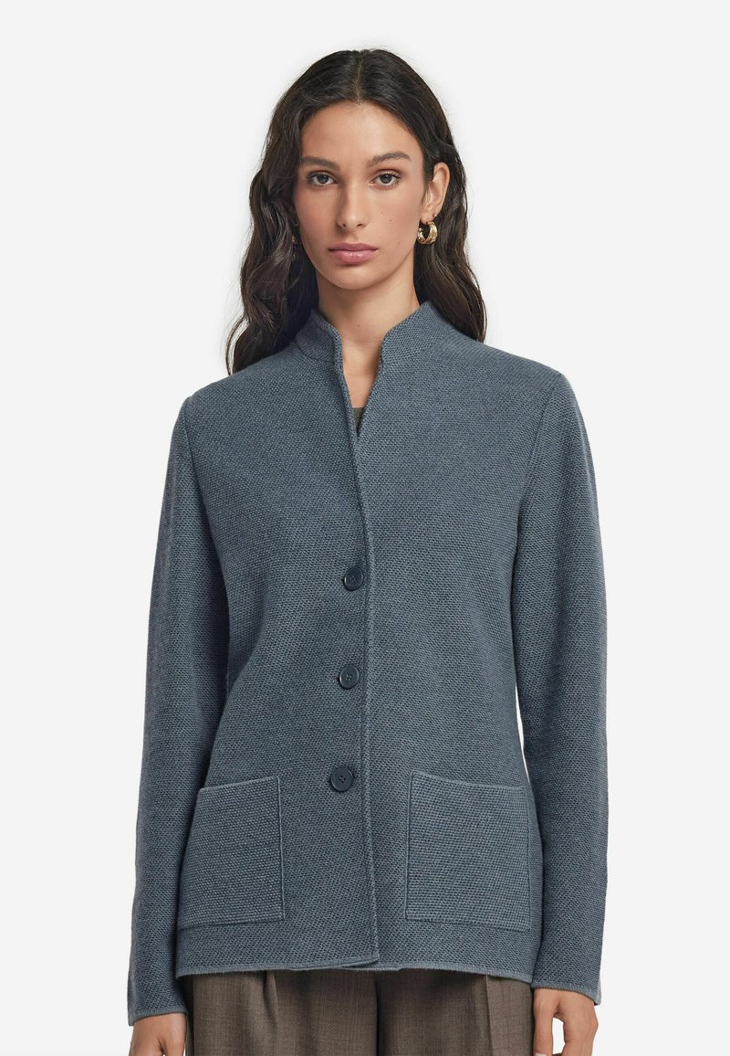 Grå texturerad cardigan med ståkrage, fyra framsnappar och två fickor. Den har en boxig passform med lång ärm.