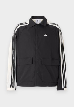 Black Adidas jacket with white sleeves, black three stripes, snap buttons down front, two front flap pockets, and logo on left chest.