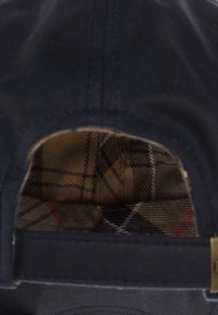 Căciulă de marină cu un exterior neted, având un căptușel cu model tartan în nuanțe de bej, maro și negru. Include o curea pentru ajustare.