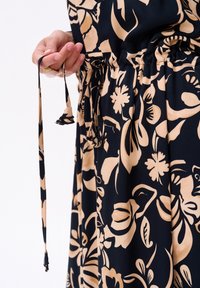 Kwiatowa sukienka na czarnym tle z beżowymi wzorami, z elastyczną talią i detalem sznurka w ręku.