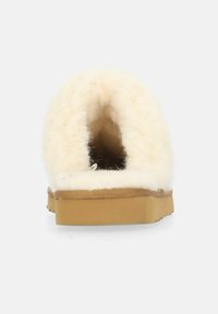 Krämfärgad toffel med en fluffig, ull-liknande textur. Har en rundad baksida, en tan-gummisula och ett mjukt inre foder.