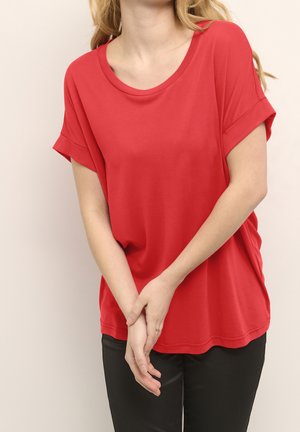 Rød kortærmet t-shirt med rund hals, blød tekstur og opkrabbede ærmer, parret med sorte bukser, der viser en afslappet pasform.