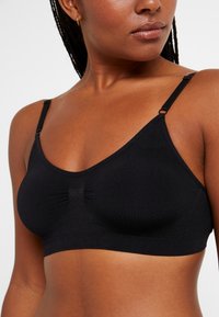Μαύρο ασύρματο σουτιέν από λείο ύφασμα, με ρυθμιζόμενους ιμάντες, συγκεντρωμένο κέντρο και χωρίς ραφές για άνεση.