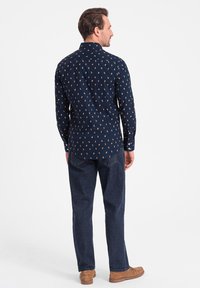 Marineblauwe blouse met lange mouwen, bedrukt met een patroon van kleine oranje vormen; kraagontwerp met knoopmanchetten, gecombineerd met donkerblauwe spijkerbroek.
