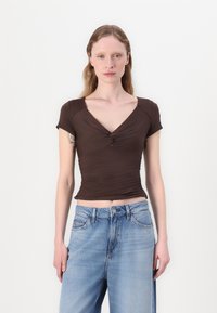 Brown short-sleeve top with a V-neck and gathered detailing, paired with light blue high-waisted jeans. Smooth texture, fitted design.