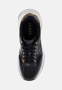 Baskets sportives noires et dorées avec textures en maille et cuir, œillets dorés, semelle intérieure et accent au talon de marque, semelle blanche avec motif de traction.