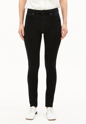 Zwarte denim skinny jeans met een hoge taille, voorzien van vijf zakken en minimale stikdetails, gecombineerd met witte veterschoenen.