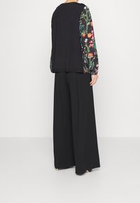Zwarte top met mouwpatronen van bloemen, gecombineerd met losse zwarte broeken. Soepele stof met een relaxte pasvorm en een ronde halslijn.